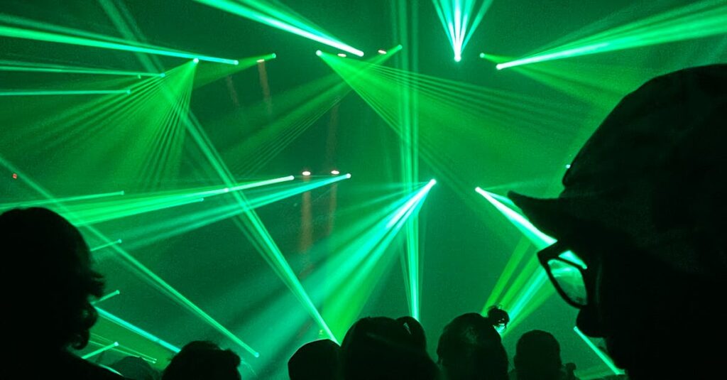 Vibrant green laser beams illuminate the night at an energetic concert or rave, creating a futuristic atmosphere.