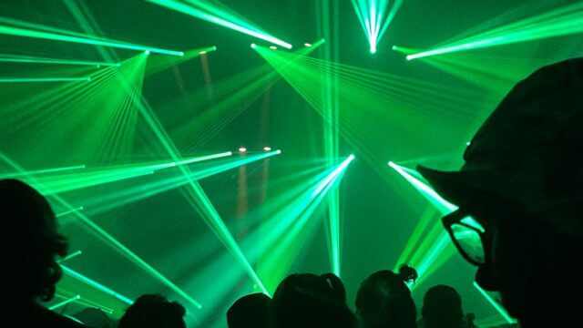 Vibrant green laser beams illuminate the night at an energetic concert or rave, creating a futuristic atmosphere.
